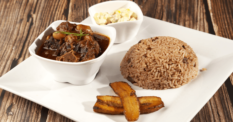 Savory oxtail served with traditional rice and peas, plantain, and macaroni salad