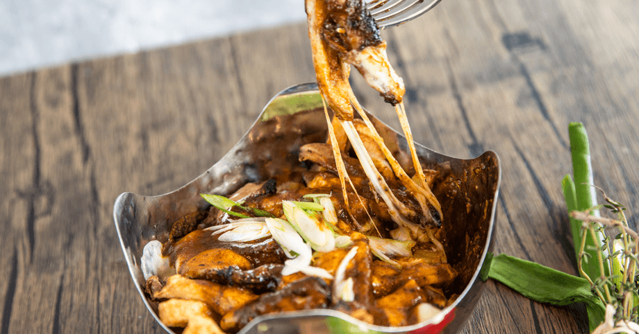 Jerk chicken poutine with melted cheese stretching from a fork