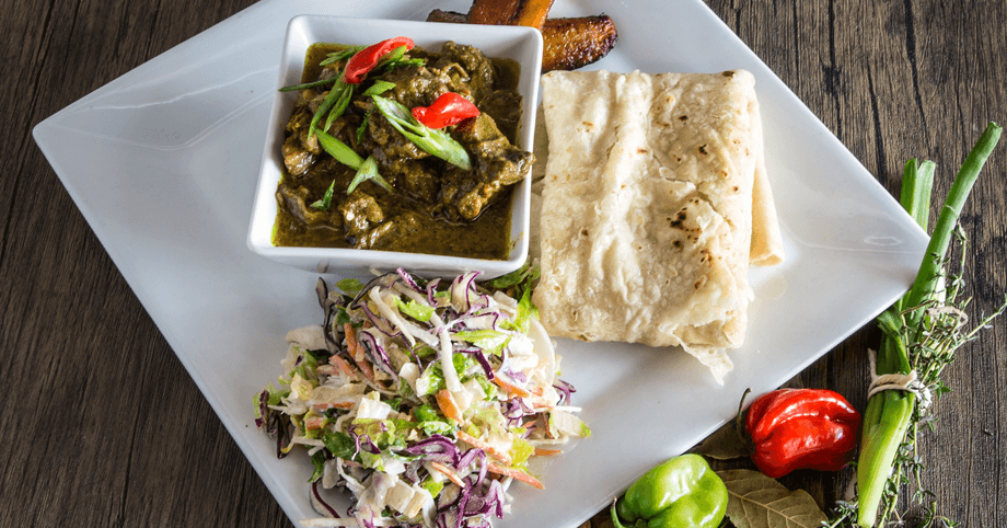 Authentic Jamaican curry goat meal with roti, fried plantain, and salad